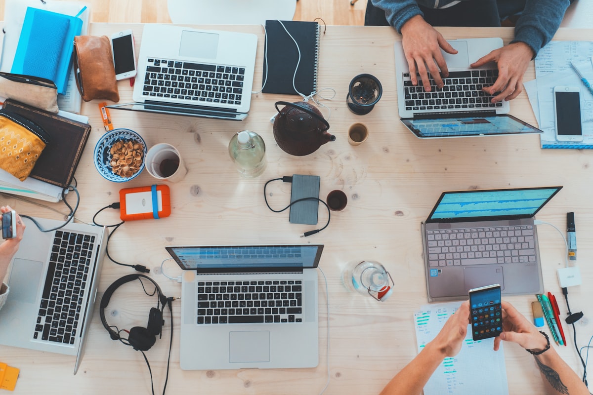 A crowded table with laptops and people working together.
